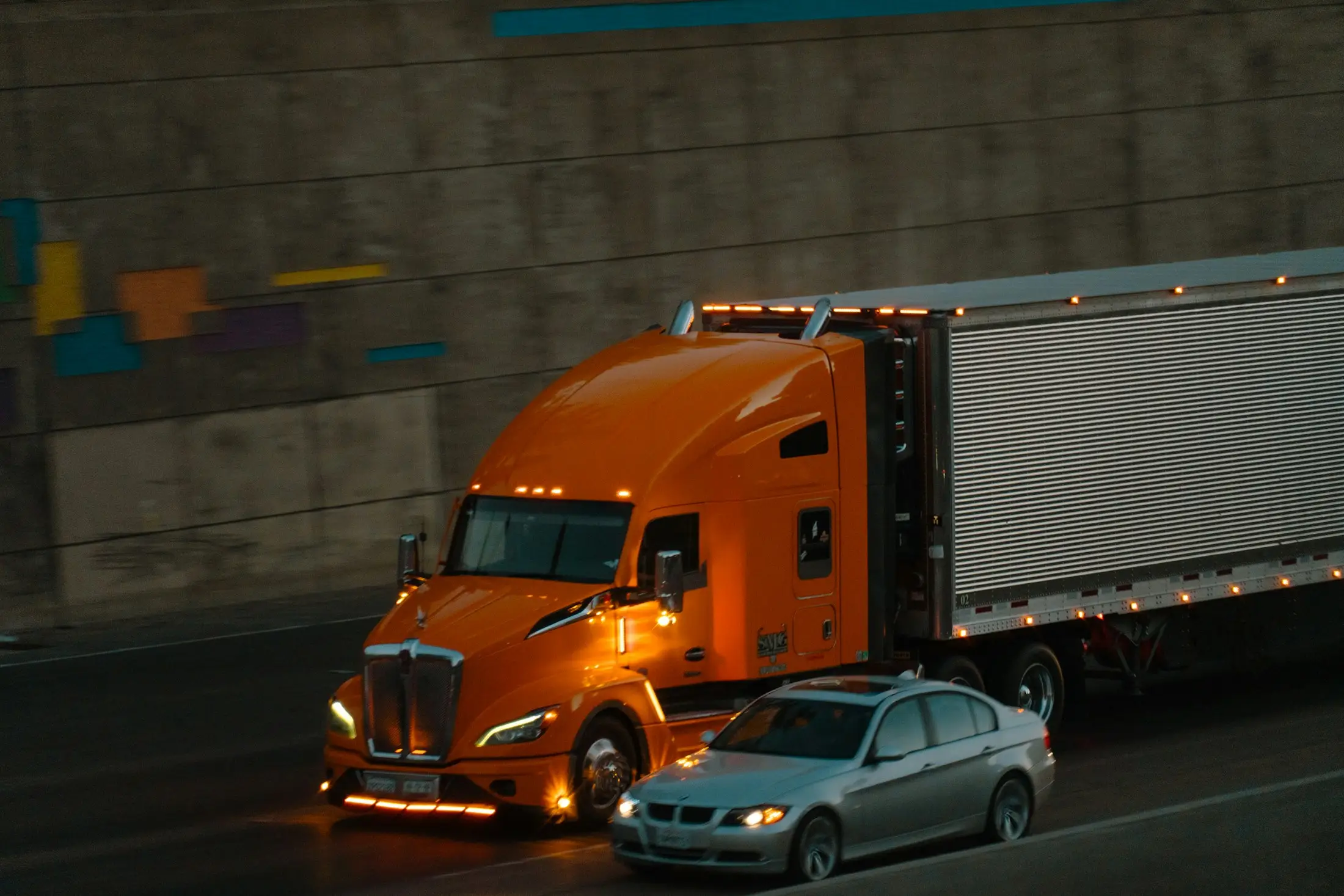 Orange Kenworth tractor pulling a reefer trailer on a highway at night