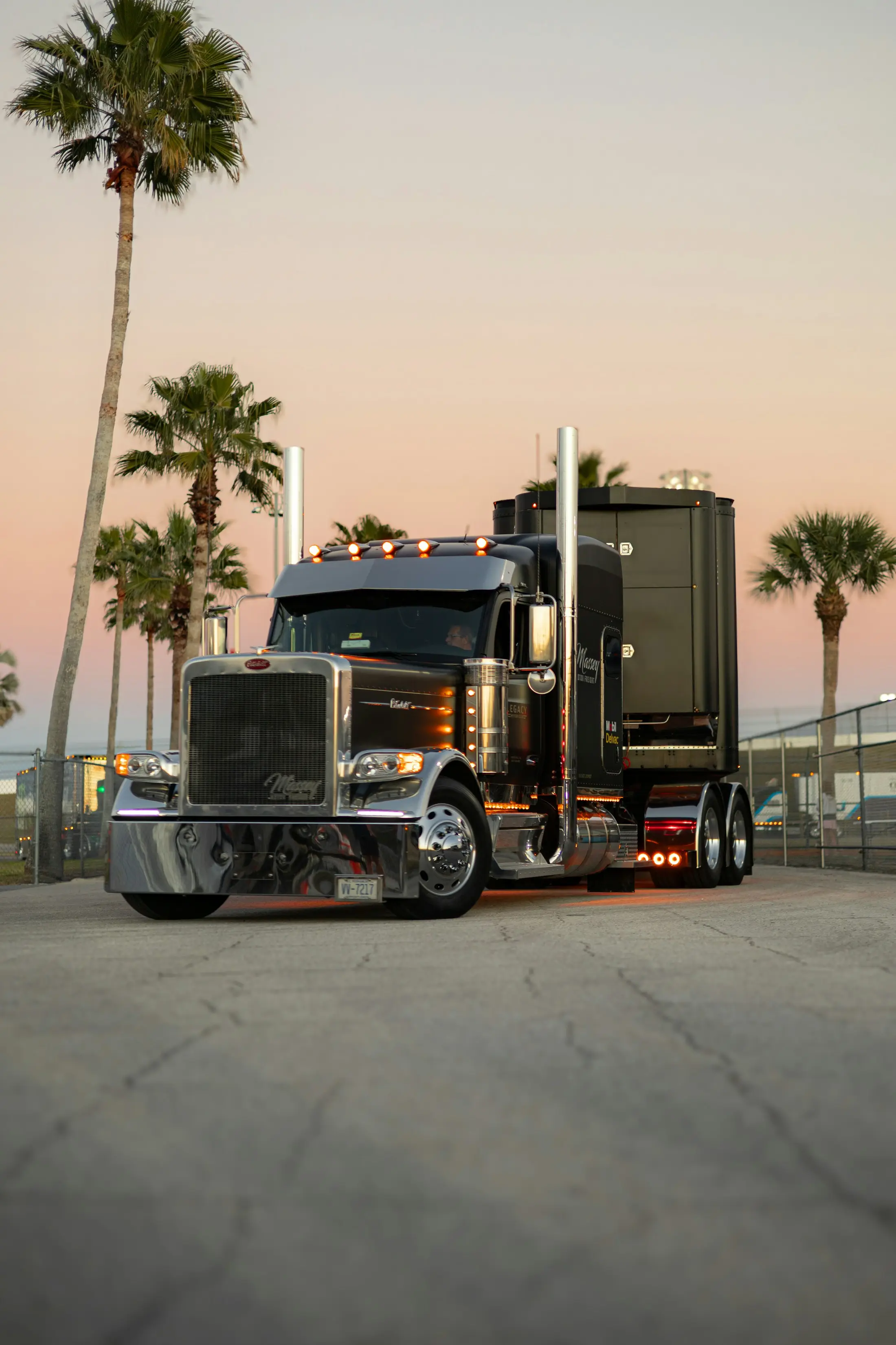 Black Peterbilt tractor parked at dusk with palm trees behind it
